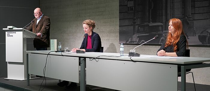 Peter Klein am Rednerpult, Lisa Hauff und Anette Daugardt sitzend auf dem Podium